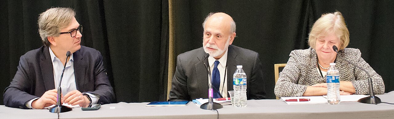 The three laureates sit at a panel table with microphones and water bottles