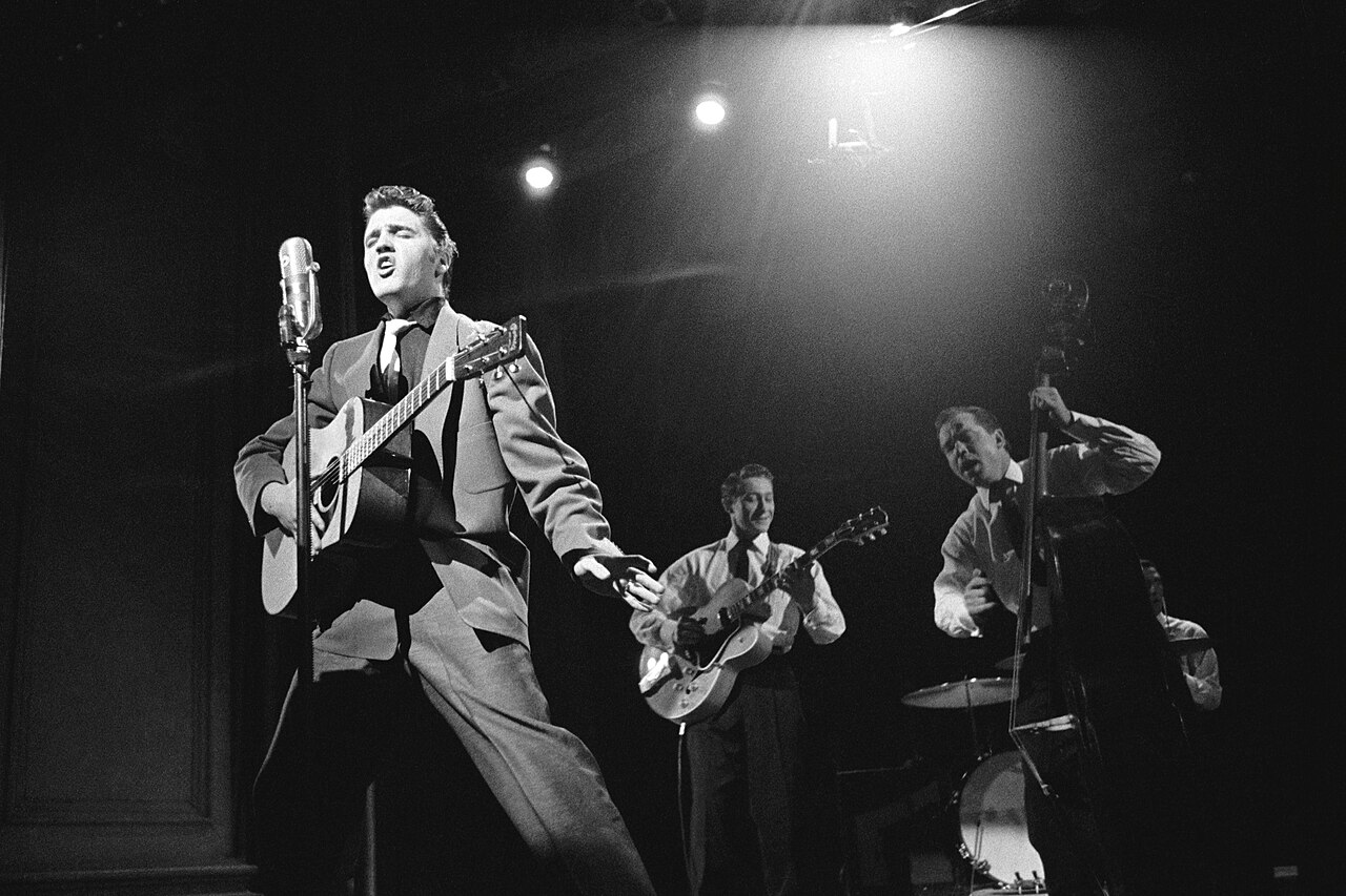 Elvis Presley performs with his band under stage lights
