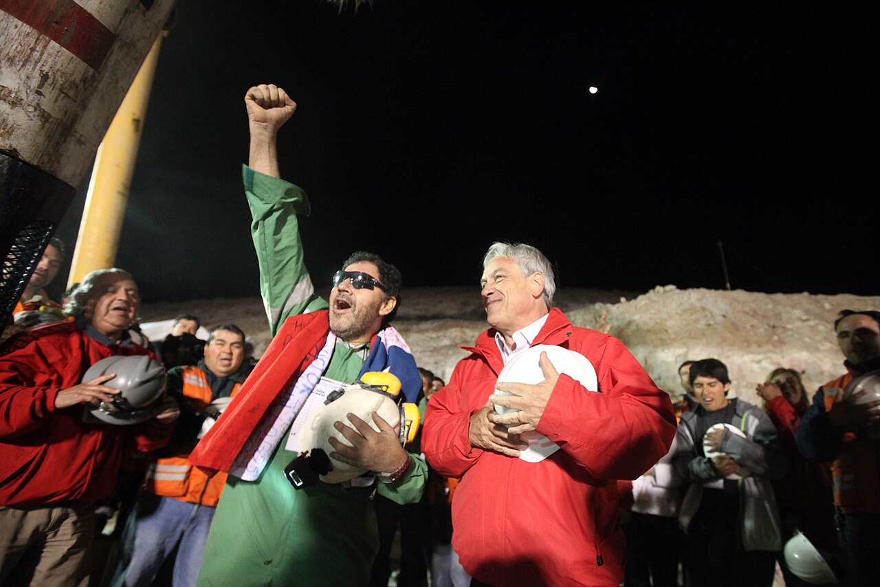 The first rescued miner raises his fist in celebration beside the president
