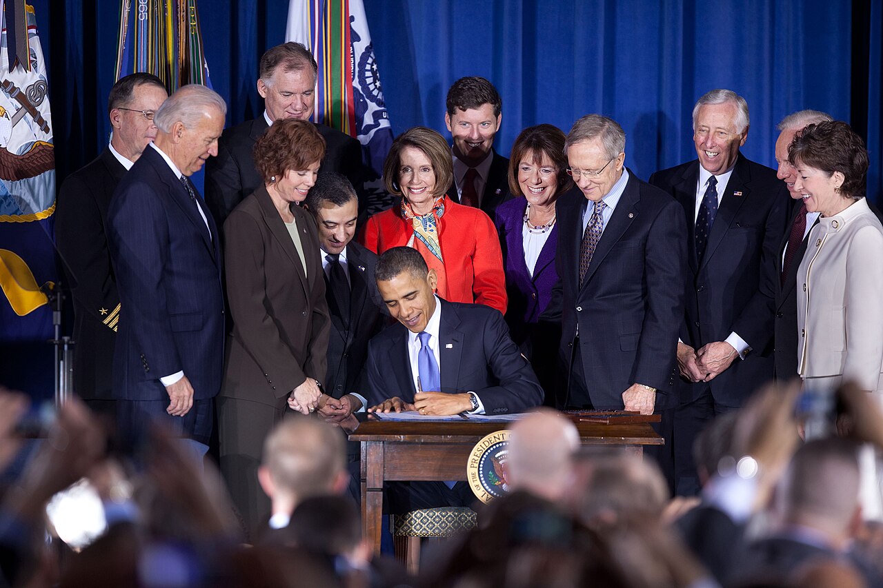 the president signs the repeal surrounded by lawmakers