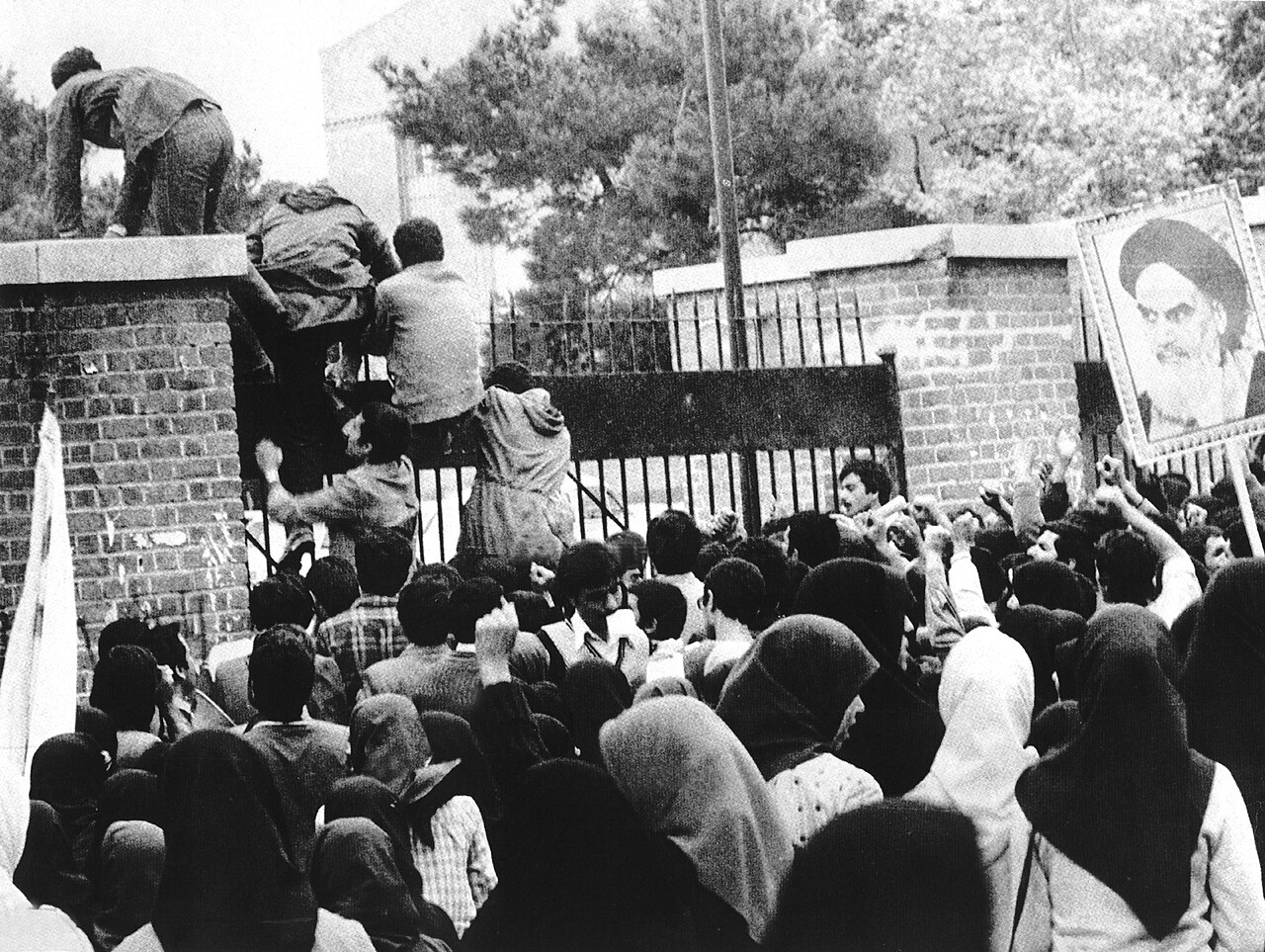 Iranian students climb the embassy wall as crowds gather below