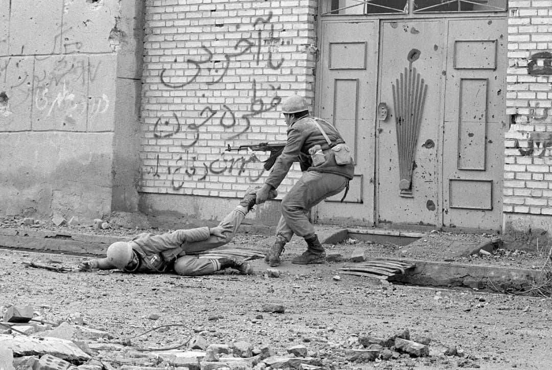 An Iraqi soldier drags a wounded comrade through a rubble-strewn street in Khorramshahr