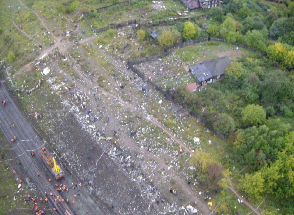 Aerial view of crash site with scattered wreckage and rescue workers below